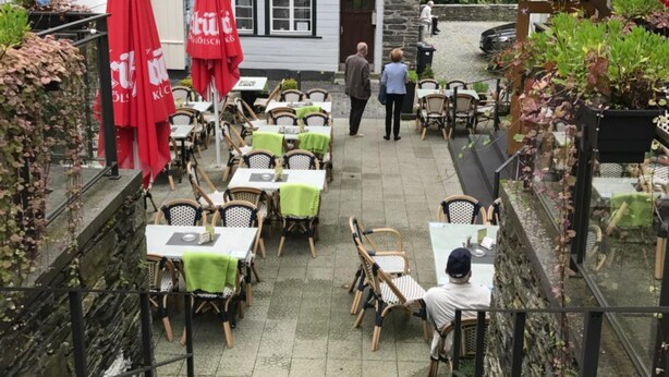 Un patio con mesas al aire libre, una escalera que sube y un edificio de fachada tradicional.