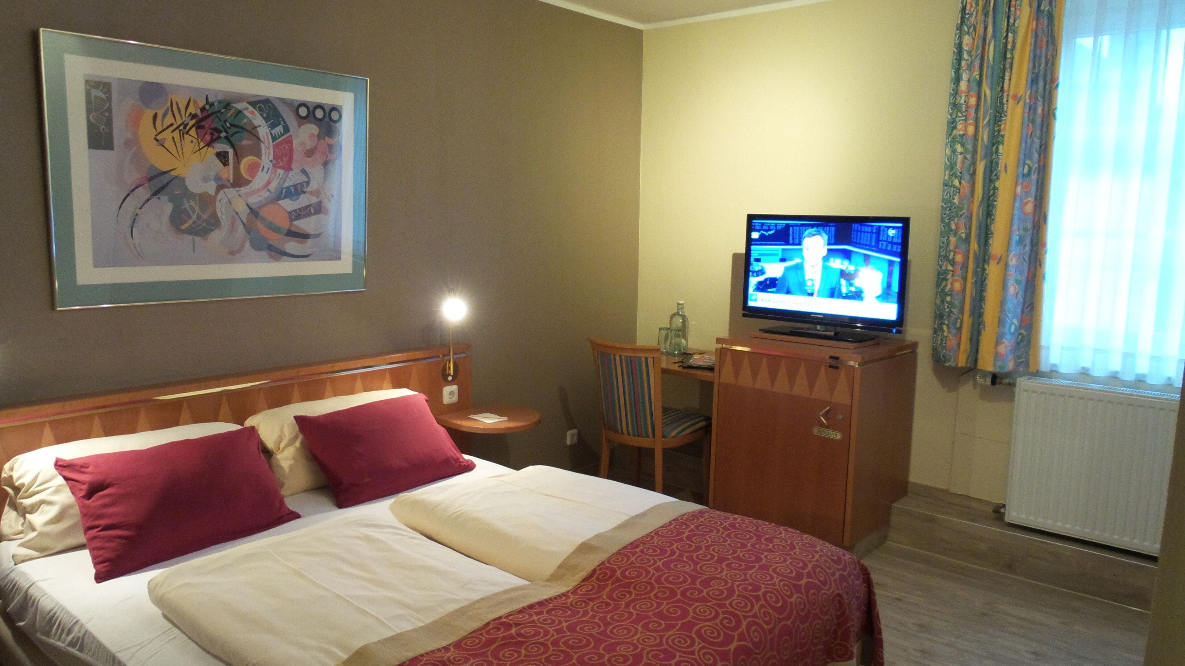 Une chambre d’hôtel avec un lit, une télévision, une petite table avec une lampe et un tableau au mur.