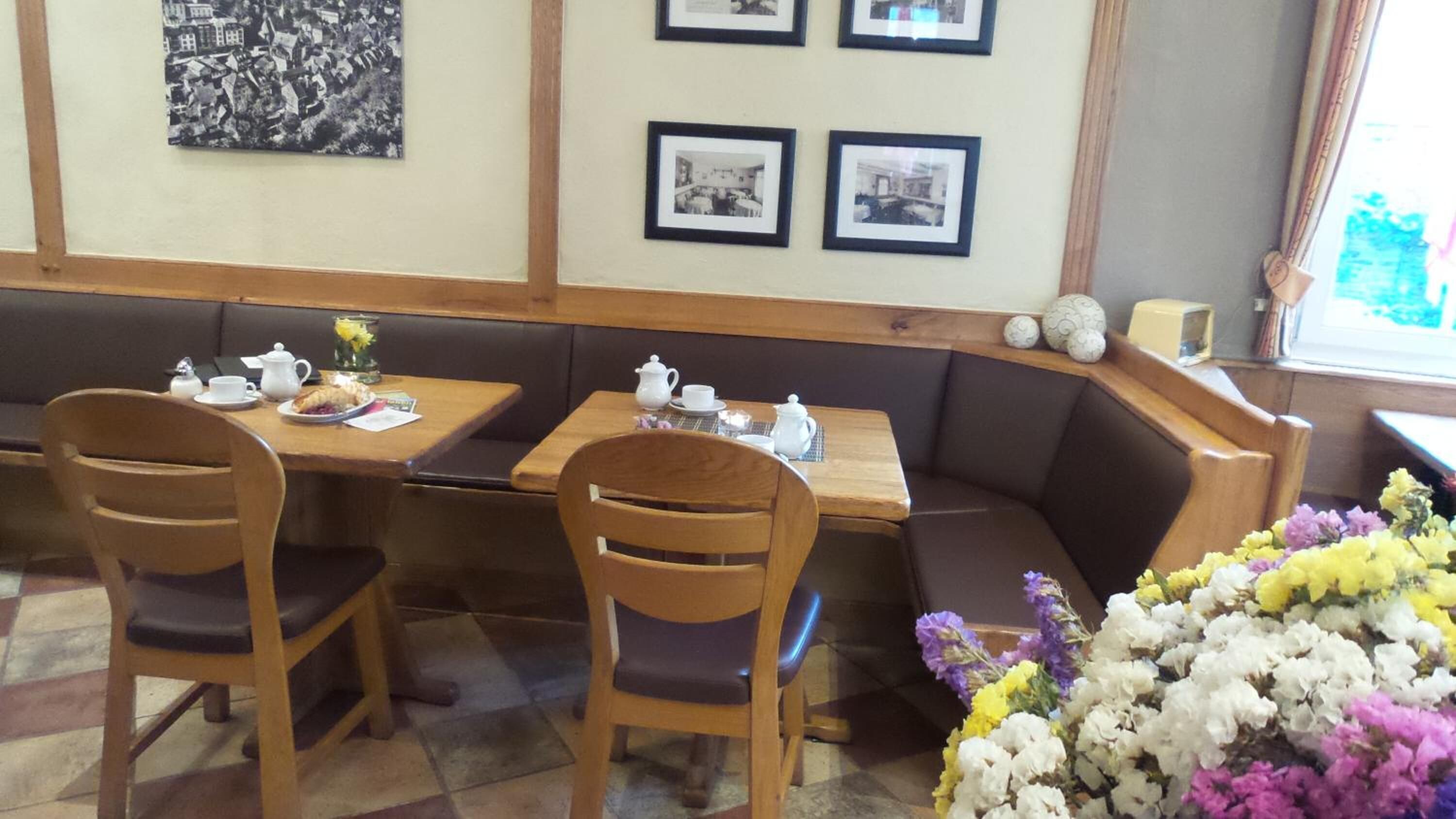 A restaurant with wooden tables and chairs, a bench seating area, and framed pictures on the wall.