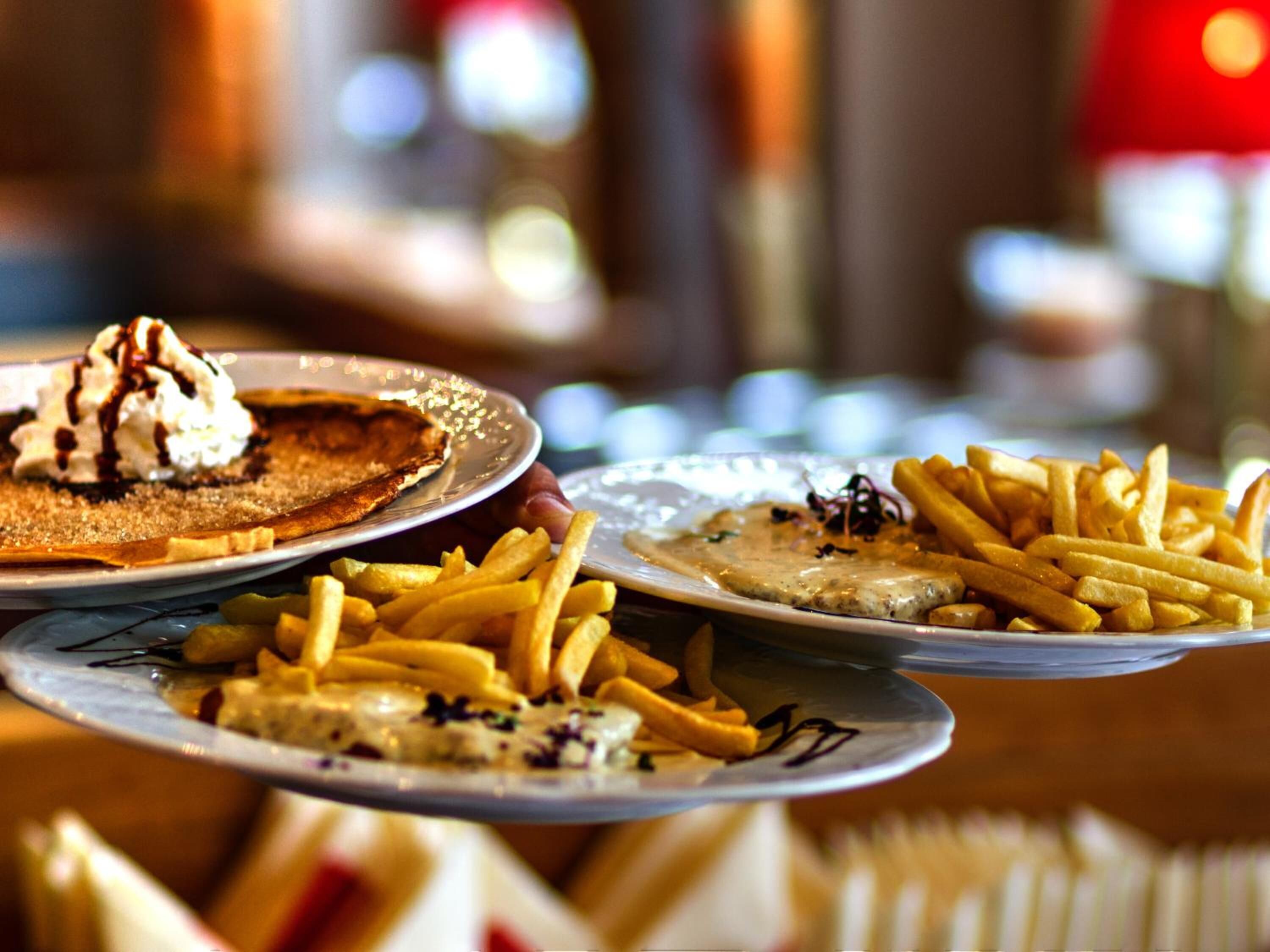 Una mesa con tres platos de comida, incluyendo panqueques con crema batida y jarabe, además de papas fritas.