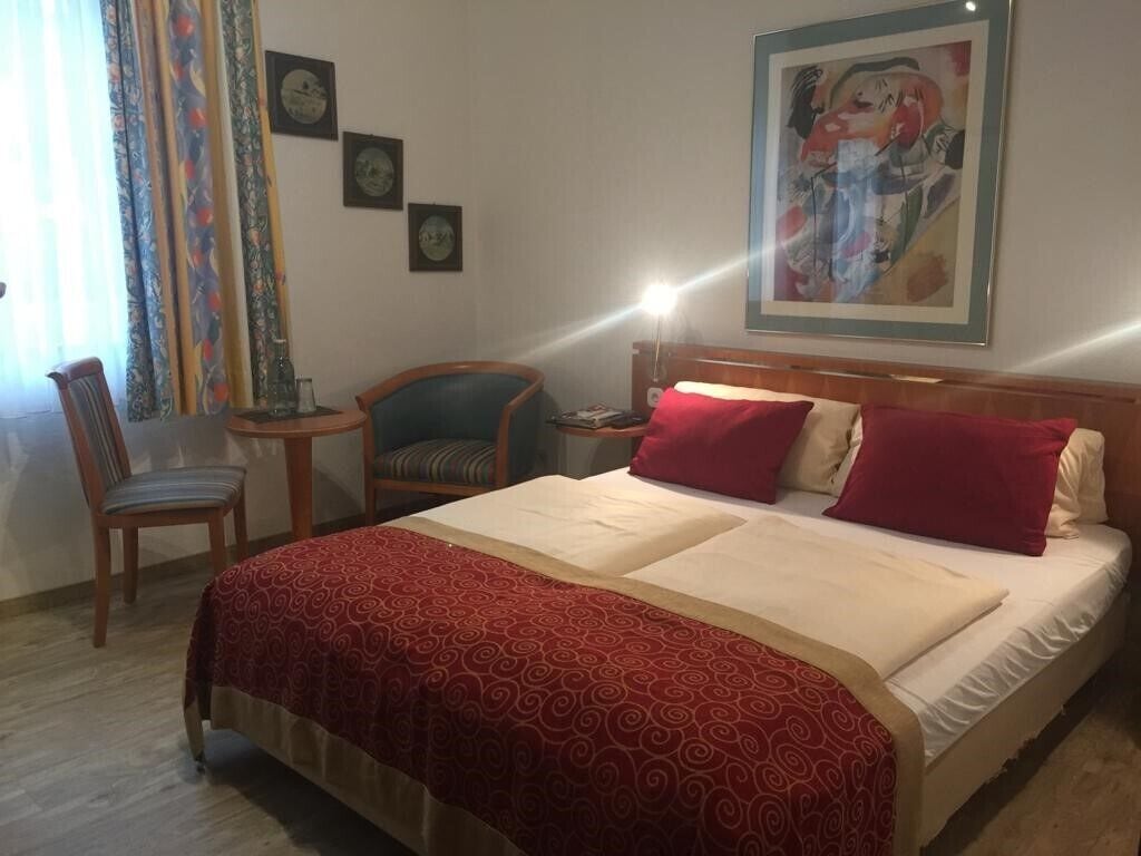 A hotel room with a large bed, two chairs, a small table, and a painting on the wall.