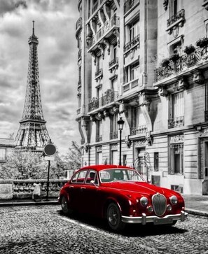 A vintage red car parked in front of a building with ornate balconies and a tower resembling the Eiffel Tower in the background. - Hôtel Pavillon des Gâtines (Plaisir)