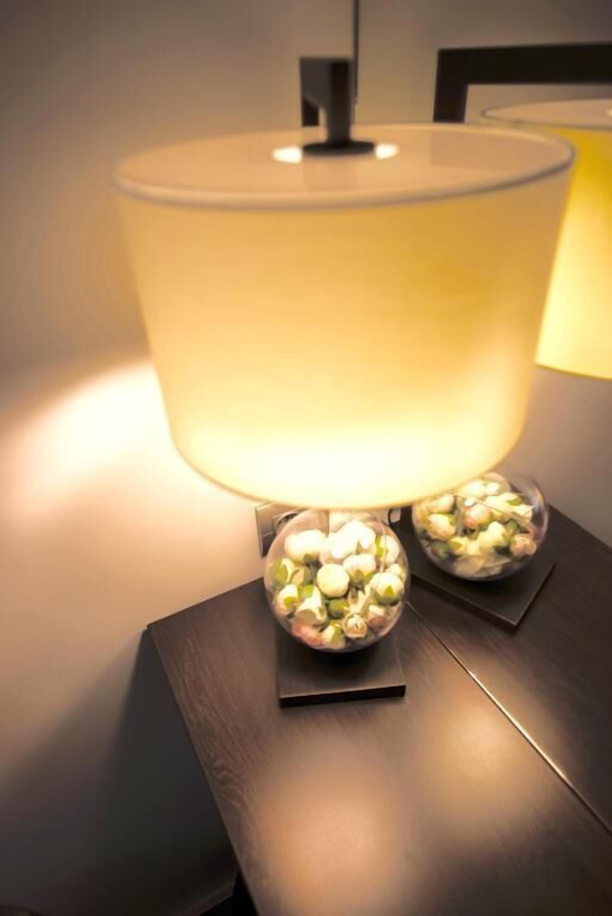 Une lampe de table dotée d’un grand abat-jour jaune doux et d’un pied comportant trois récipients sphériques en verre remplis de petits cailloux.