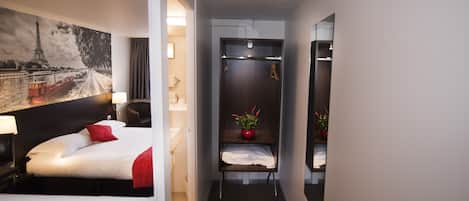 Habitación de hotel con cama, mesita de noche, espejo, una pequeña mesa con un florero y vistas a la Torre Eiffel.