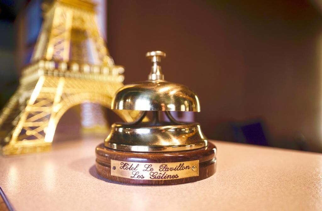 A hotel bell with a wooden base and a metal top, labeled "Hotel Le Pavillon Les Gâtines."