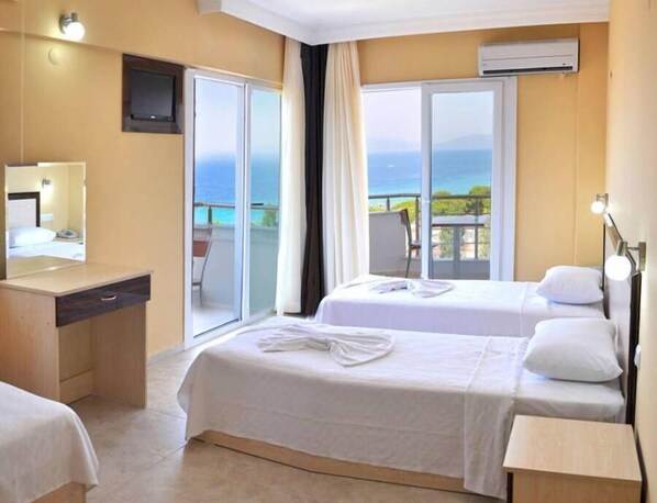 Ein Hotelzimmer mit zwei Betten, einem Schreibtisch, einem Spiegel und einem Balkon mit Meerblick.
