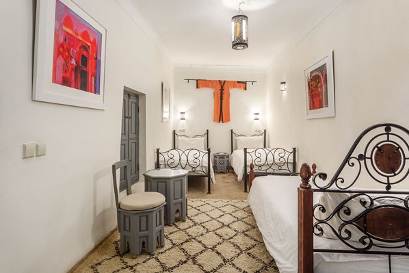 A bedroom with two beds, a chair, a small stool, and a framed painting on the wall.
