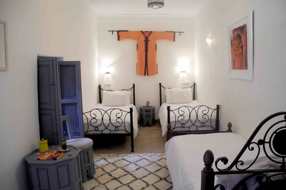 A bedroom with two beds, a small table, a wardrobe, and a patterned rug.