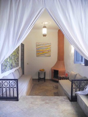 Una habitación acogedora con una cama, una mesita con fruta, una chimenea y un cuadro en la pared.