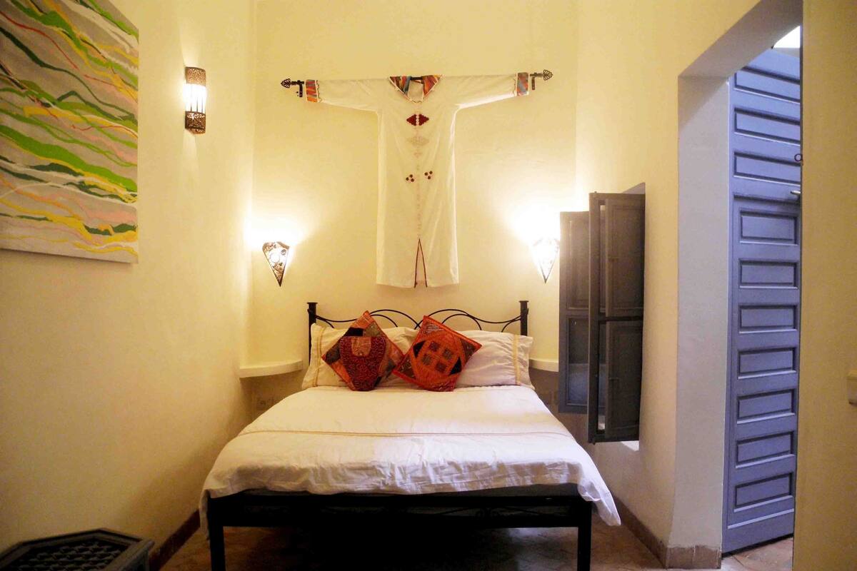 A bedroom with a bed, a wall-mounted light fixture, a door, and a patterned rug.