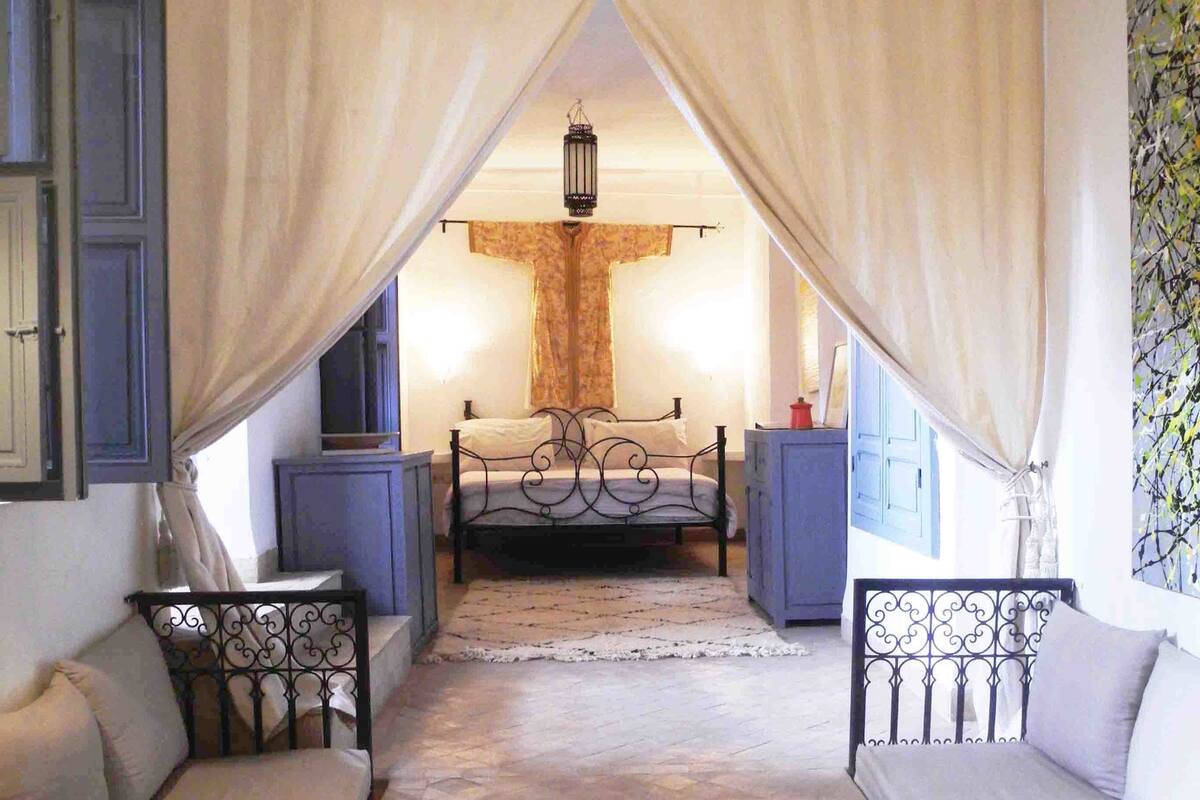 A bedroom with a bed, a nightstand, a chair, and a staircase leading to a balcony.