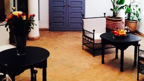 A room with a blue door, a potted plant, a chair, a table with fruit, and a hanging light fixture. - Riad Linda (Marrakech)