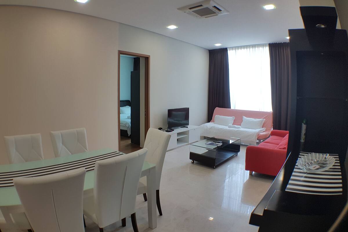 Una habitación de hotel moderna con zona de comedor, sofá, televisor y cama.