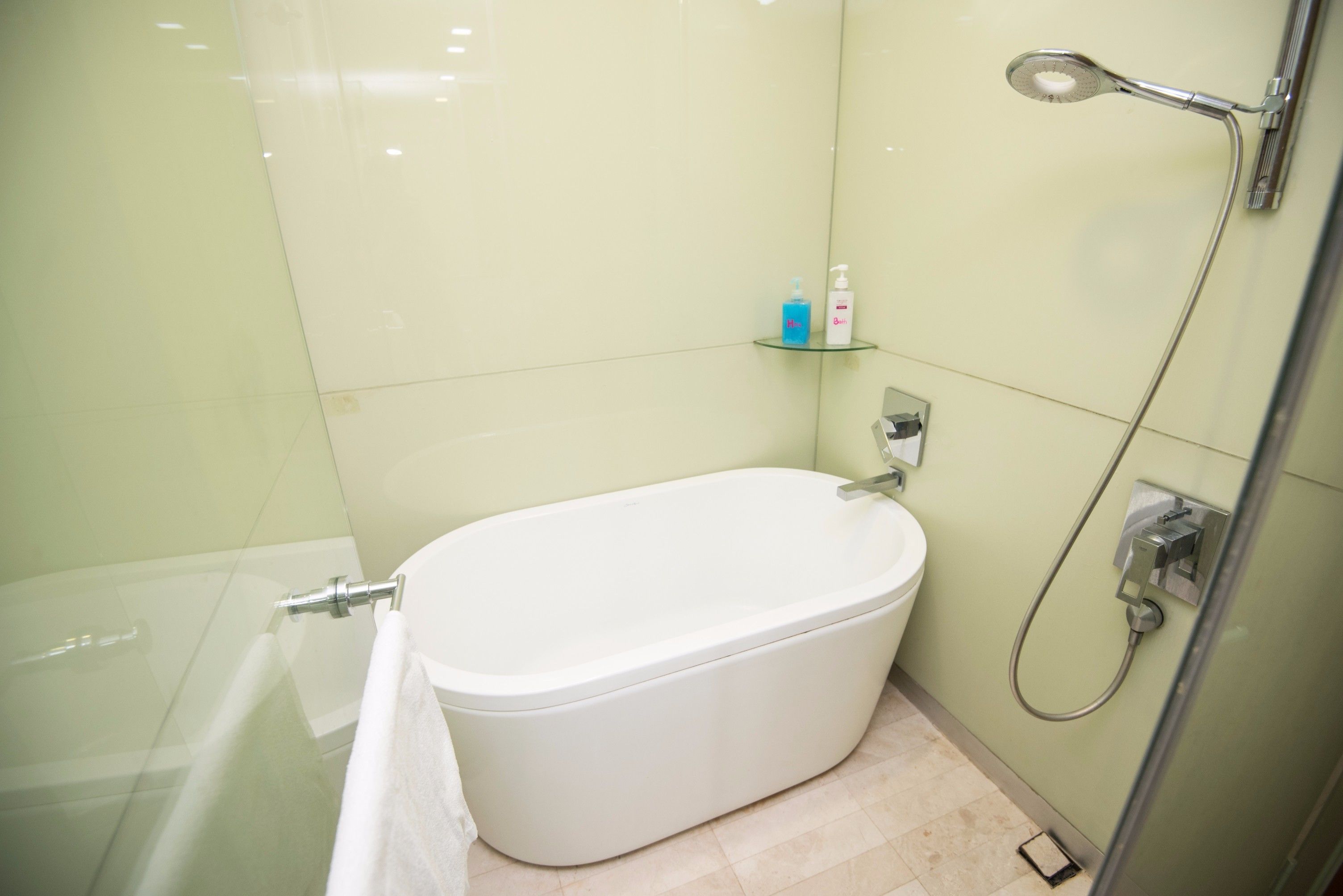 Een badkamer met een witte badkuip, een douchecabine van glas en een plank met toiletartikelen.