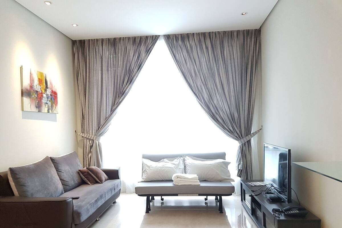 Una sala de estar moderna con un sofá, un banco y un televisor sobre un mueble bajo.