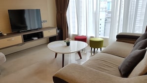Ein modernes Wohnzimmer mit Flachbildfernseher, rundem Couchtisch, beiger Couch und zwei Hocker.
