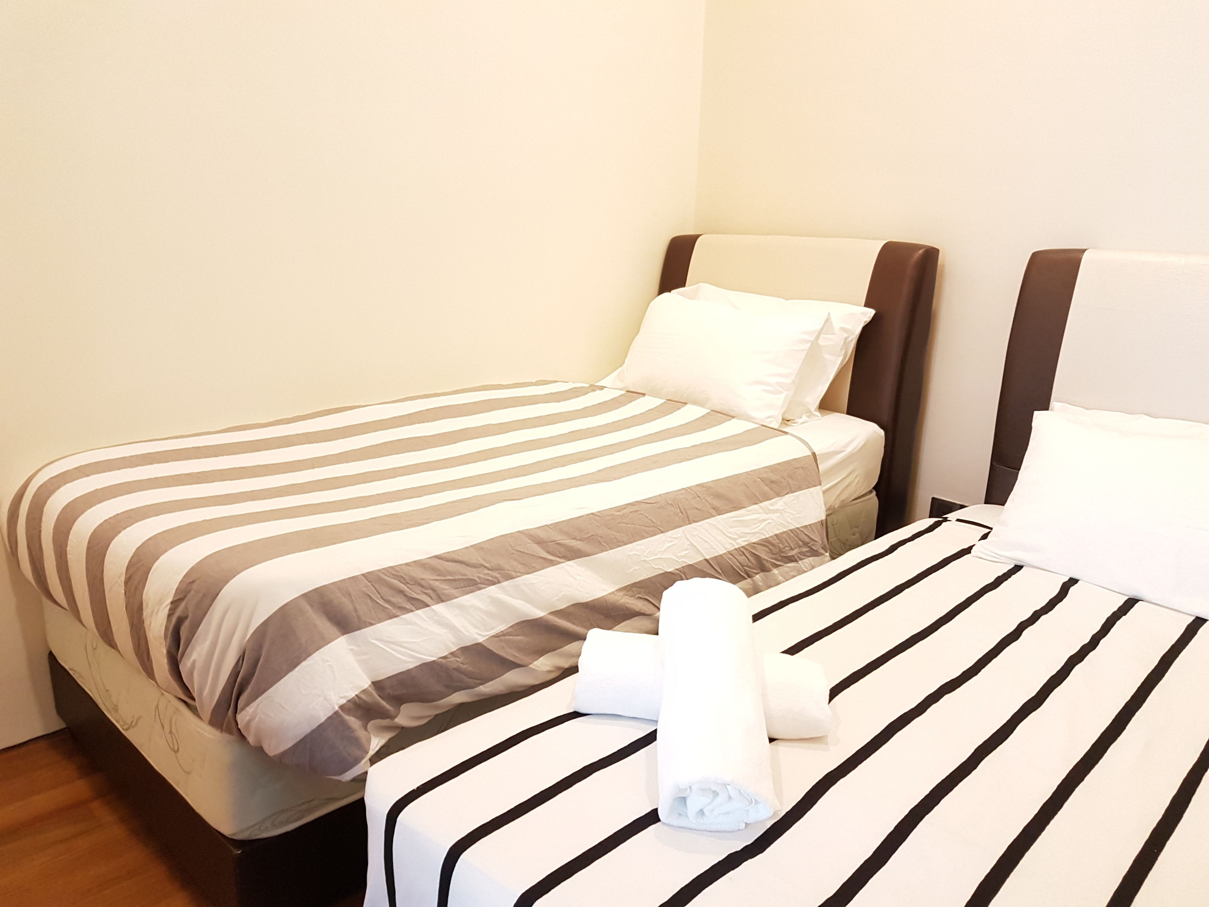 A hotel room with two beds, each with striped bedding and a rolled towel on one bed.