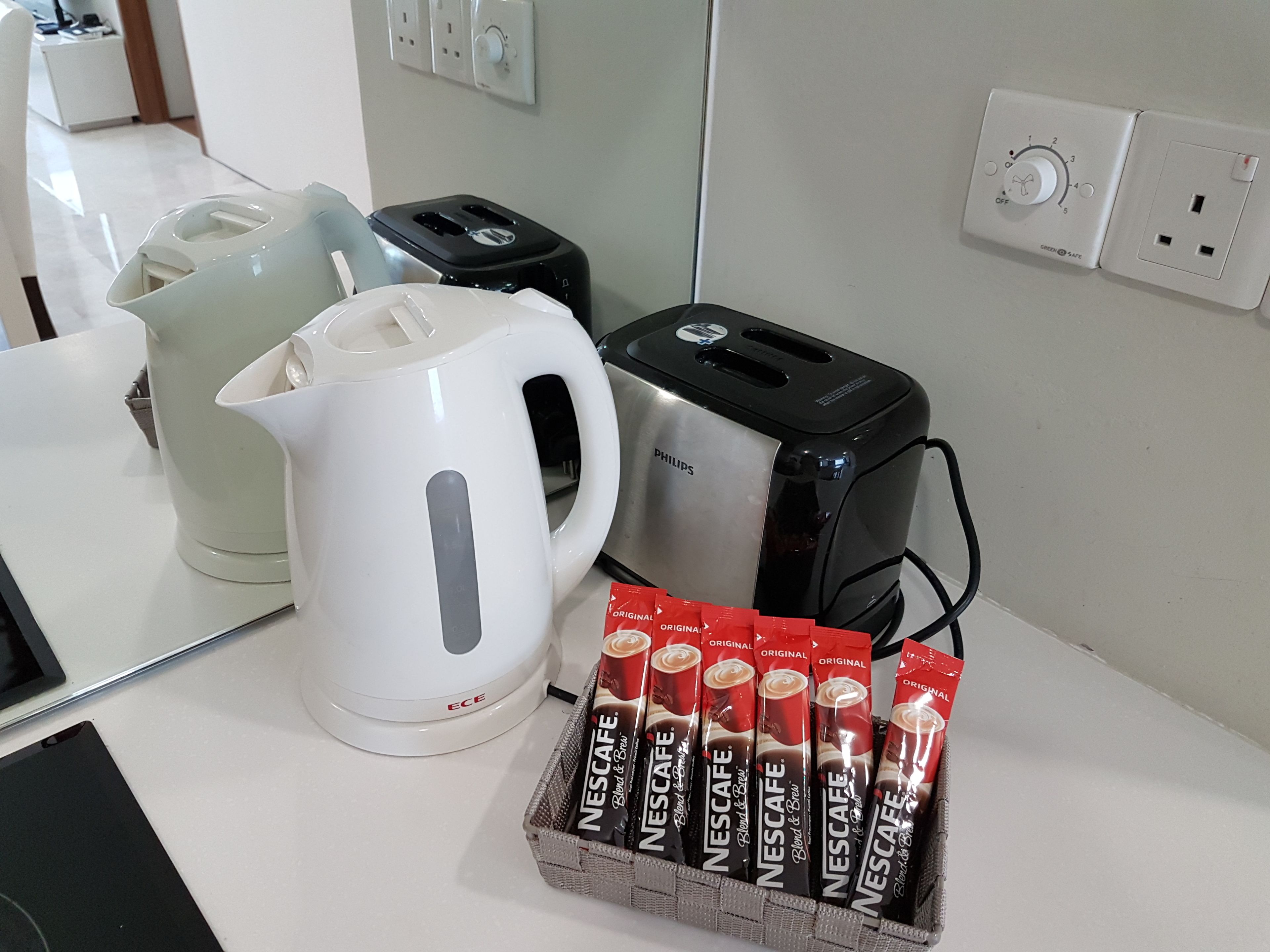 A kitchen counter with a white electric kettle, a black Philips toaster, and a carton of Nescafe instant coffee.