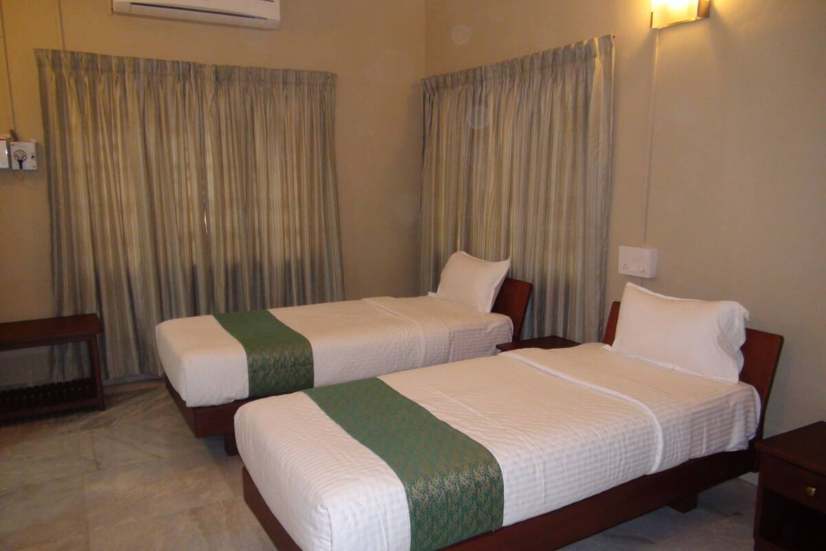 Ein Hotelzimmer mit zwei Einzelbetten, einem Holfnachtkästchen, einem Schreibtisch und einem Stuhl.