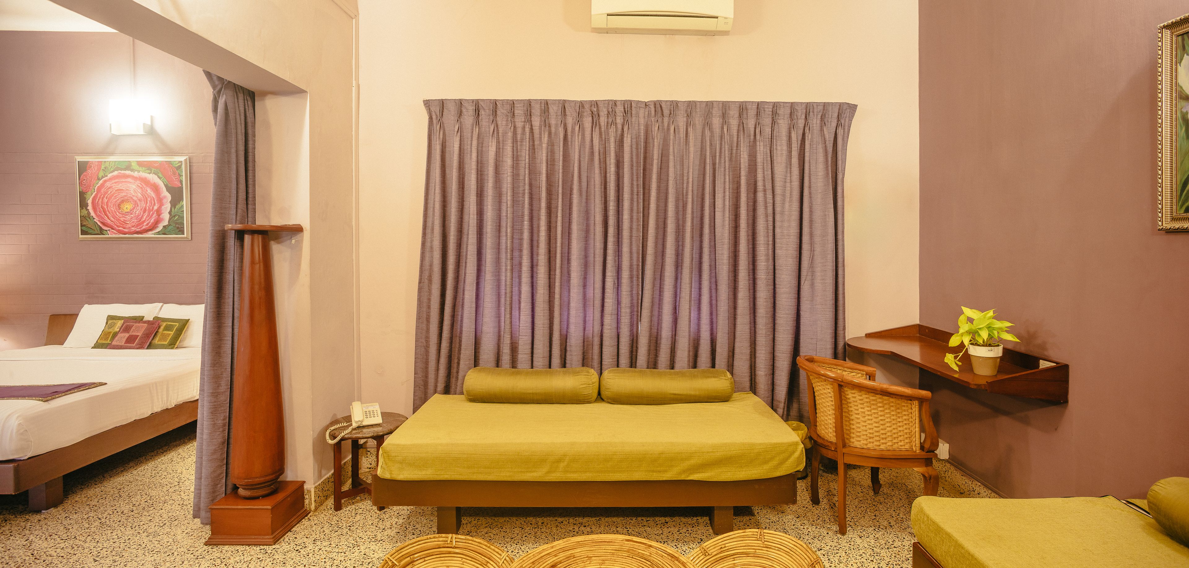 A hotel room with a bed, bedside table, lamp, chair, and a shelf with a plant.