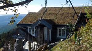 A traditional wooden building with a thatched roof, a wooden staircase, and a sign reading "VELKOMMEN". - Norefjellhytta  (Krodsherad)