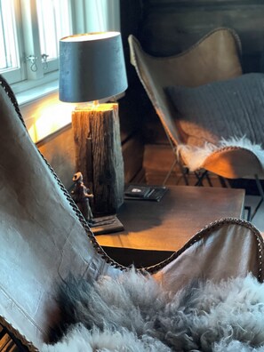 A chair with a fur throw, a lamp on a wooden base, and a small statue on a table. - Norefjellhytta  (Krodsherad)