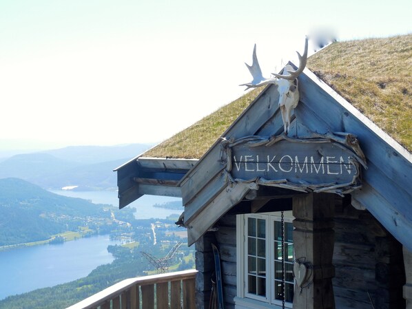 A wooden cabin with a 'Welcome' sign, a window, and a view of a lake and mountains. - Norefjellhytta  (Krodsherad)