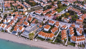 An aerial view of a coastal residential area with houses, a beach, and a clear sky. - Greek Pride Ηotel and Apartments (Kassandra)