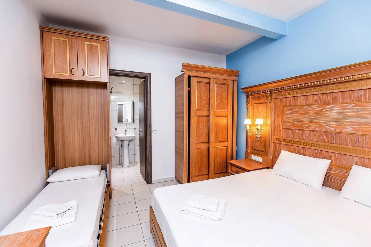 A hotel room with two beds, wooden wardrobes, a bathroom with a sink, and a mirror.