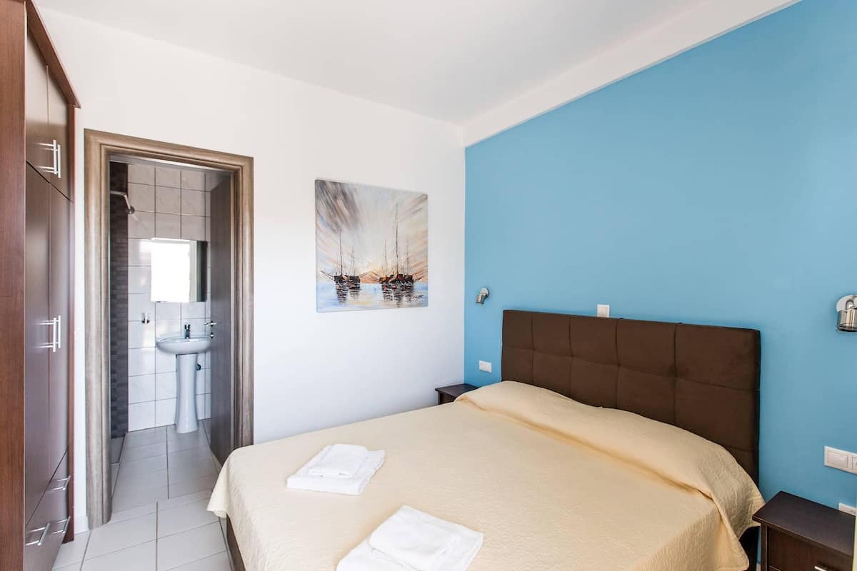 A hotel room with a bed, a painting, a bathroom, and a blue wall.