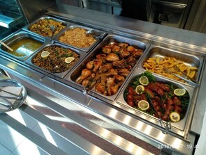 A buffet with various dishes including rice, chicken, and salads.