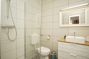 A modern bathroom with a glass-enclosed shower, a white toilet, a sink with a wooden countertop, and a mirror above the sink. - Ferienhus Baabe (Ostseebad Baabe)