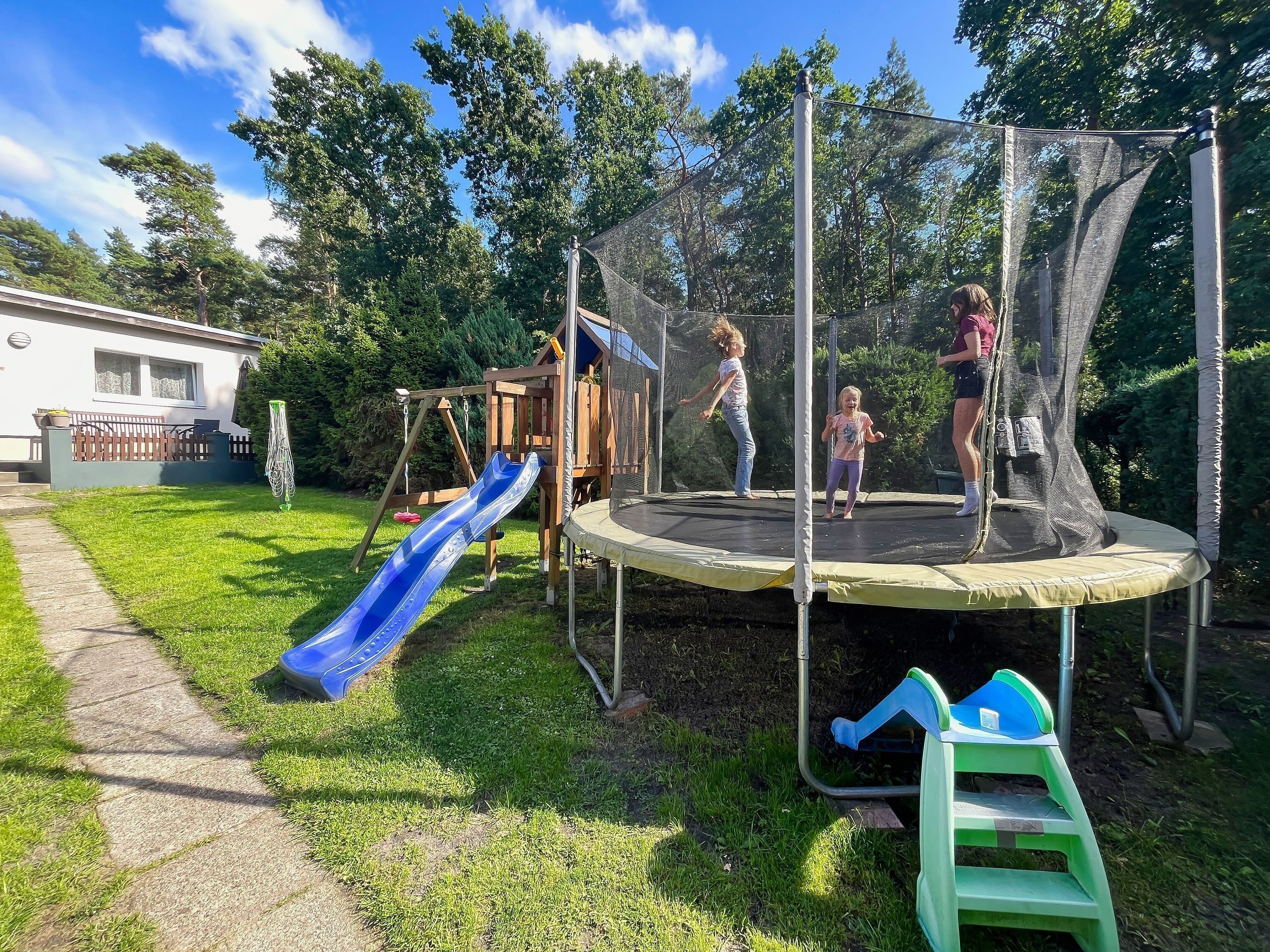 Un parque infantil con un trampolín, tobogán y columpios.