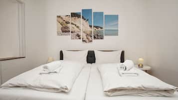 A double bed with white linens, a headboard, bedside lamps, and a wall-mounted artwork depicting a coastal scene.