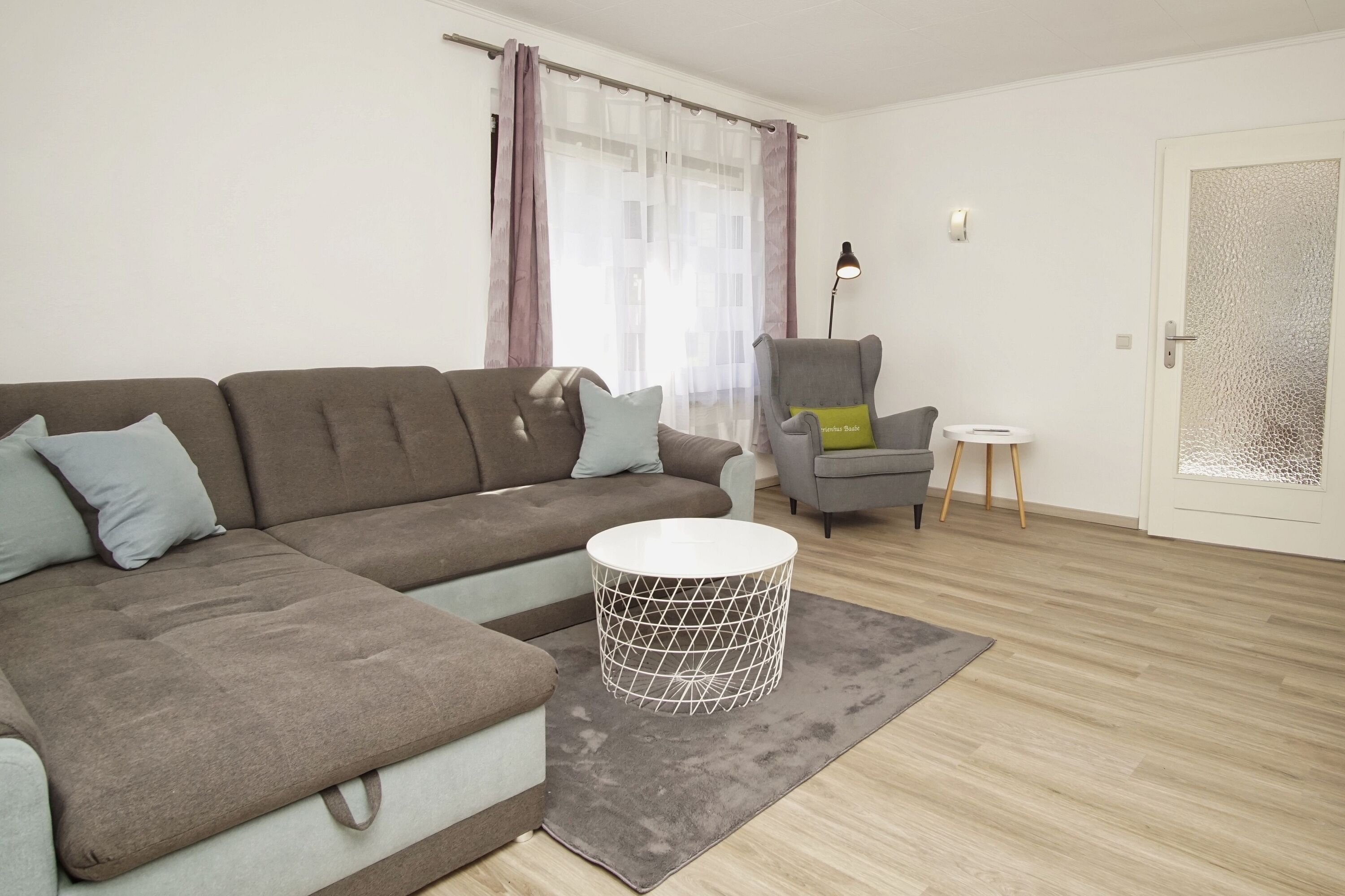 Una sala de estar moderna con un sofá modular, una mesita redonda, un sillón gris y una pequeña mesa auxiliar.
