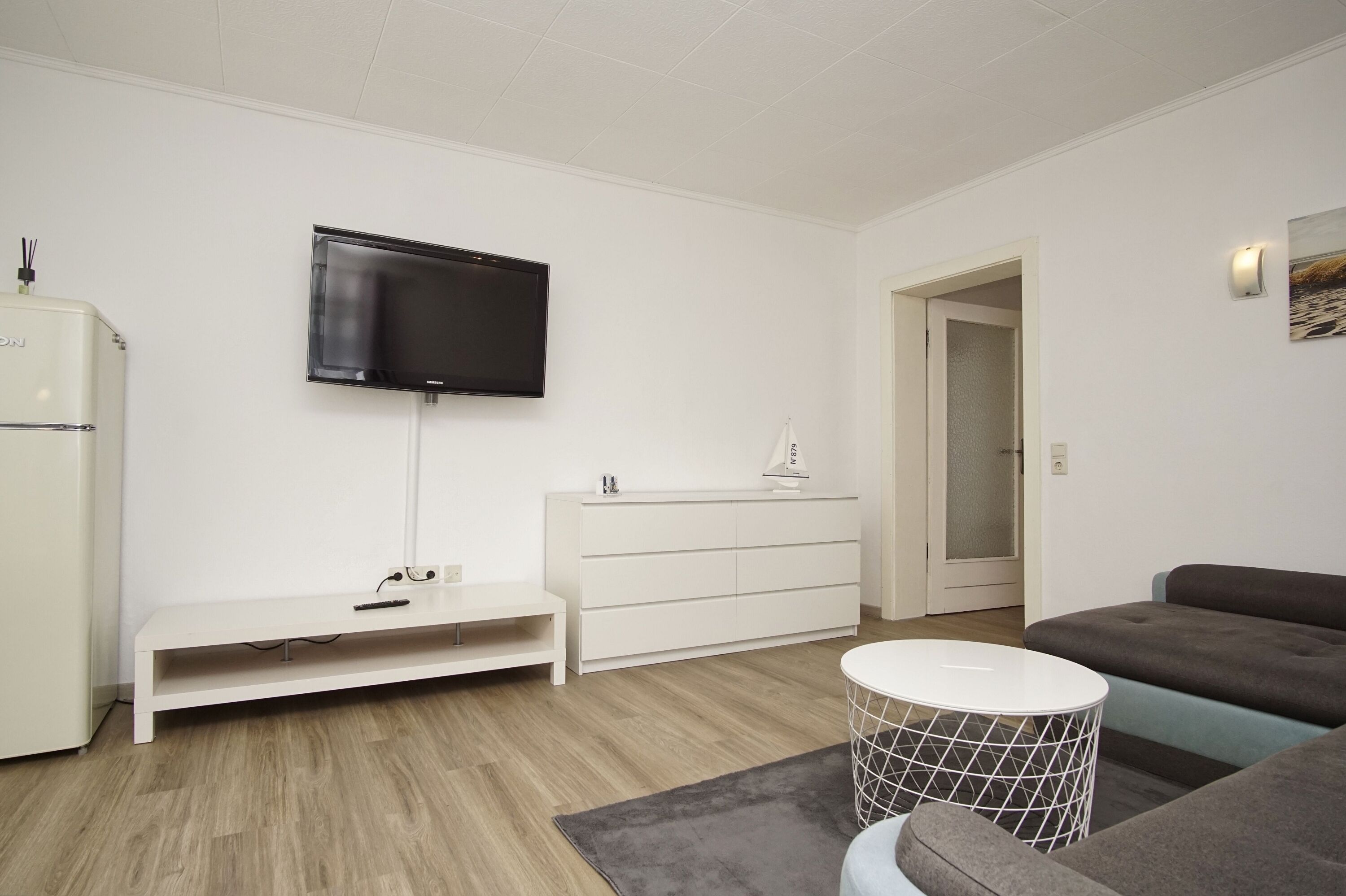 A modern living room with a flat-screen TV, white furniture, a grey sofa, and a round coffee table.