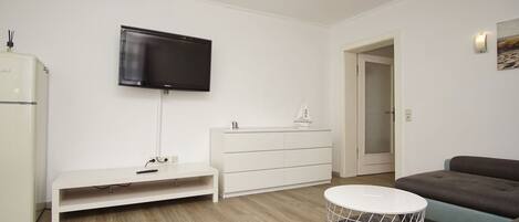 A modern living room with a flat-screen TV, white furniture, a grey sofa, and a round coffee table.