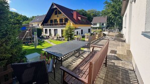 A residential area with a house featuring a balcony, a paved patio with a table and chairs, and a well-maintained lawn. - Ferienhus Baabe (Ostseebad Baabe)