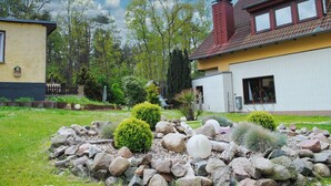 A residential property with a well-maintained garden, a stone pathway, and a red-roofed house. - Ferienhus Baabe (Ostseebad Baabe)