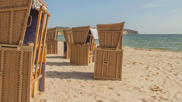 Wicker beach chairs lined up on a sandy beach with a clear view of the sea and a distant rocky outcrop. - Ferienhus Baabe (Ostseebad Baabe)