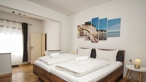 A bedroom with a wooden bed, white bedding, a bedside table with a lamp, and a wall with three landscape paintings. - Ferienhus Baabe (Ostseebad Baabe)