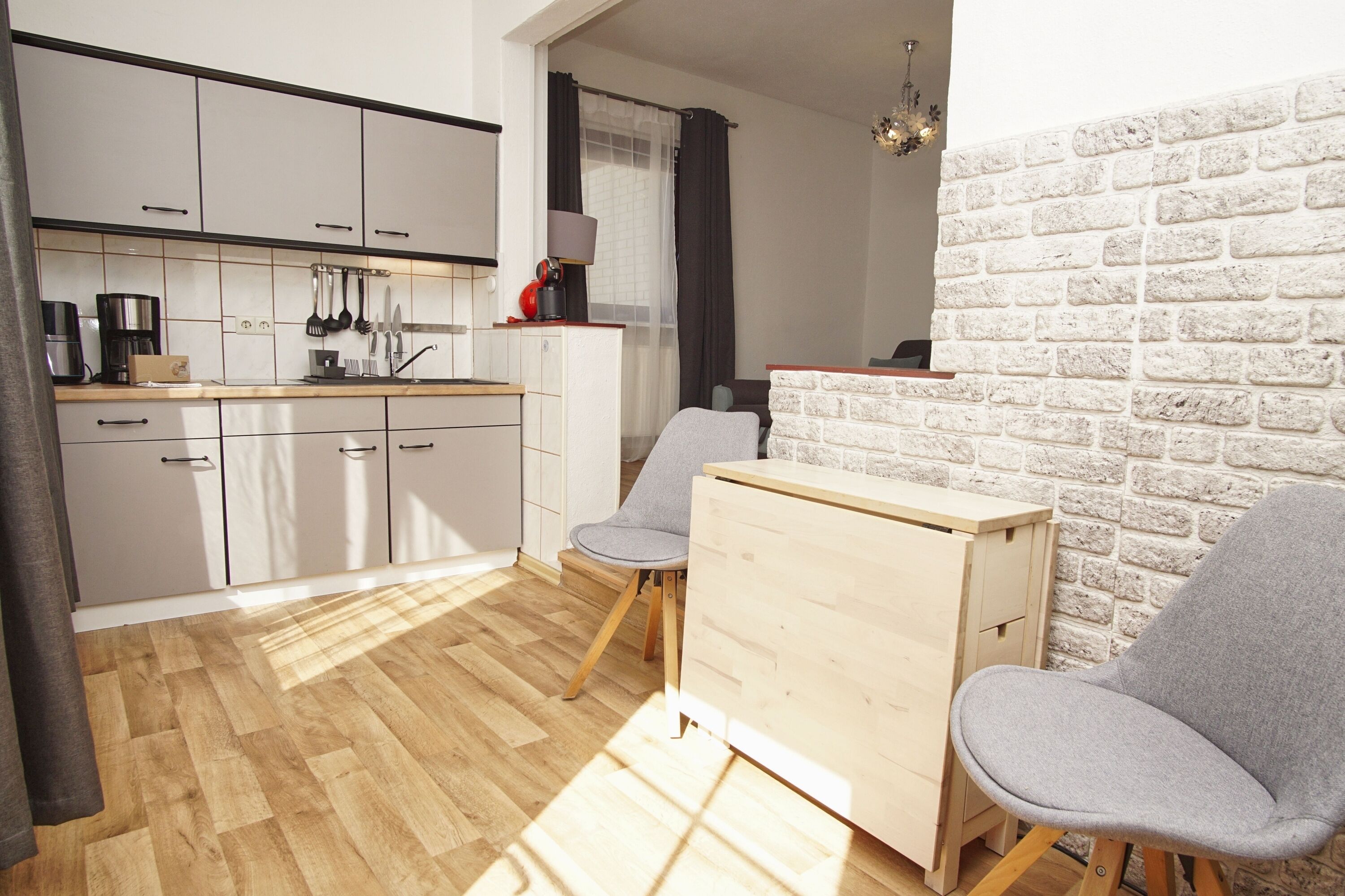 Cocina compacta con armarios blancos, encimera de madera y un pequeño comedor con dos sillas y una mesa.