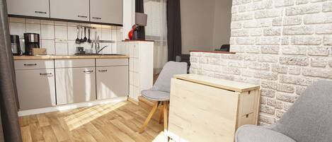 Cocina compacta con armarios blancos, encimera de madera y un pequeño comedor con dos sillas y una mesa.