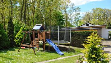 Een speeltuin met een glijbaan en schommels, omringd door bomen en een huis op de achtergrond.