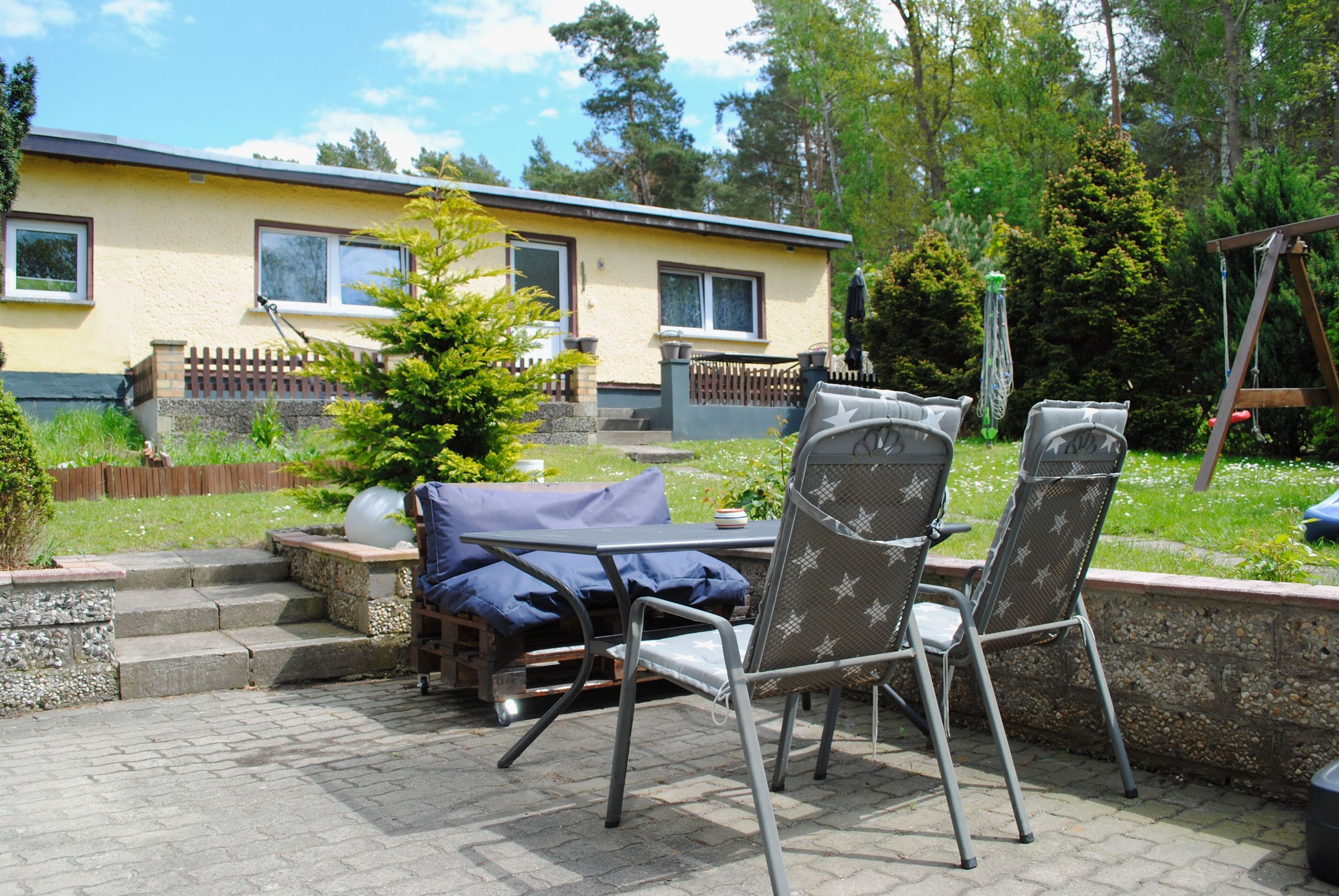 A patio with two chairs, a table, and a small tree.