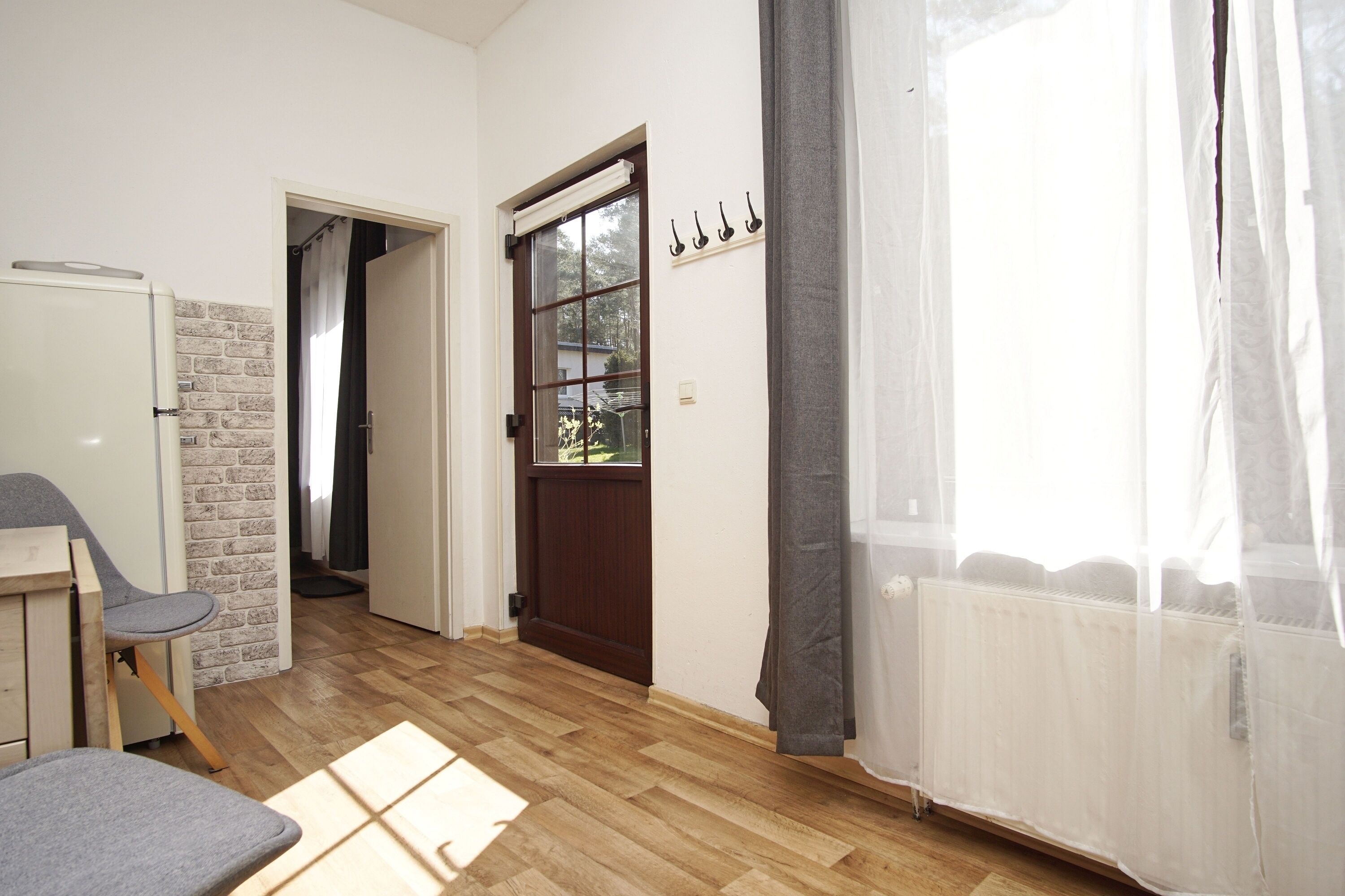 Una habitación con piso de madera, una puerta que da al exterior, un radiador y una ventana con cortinas.
