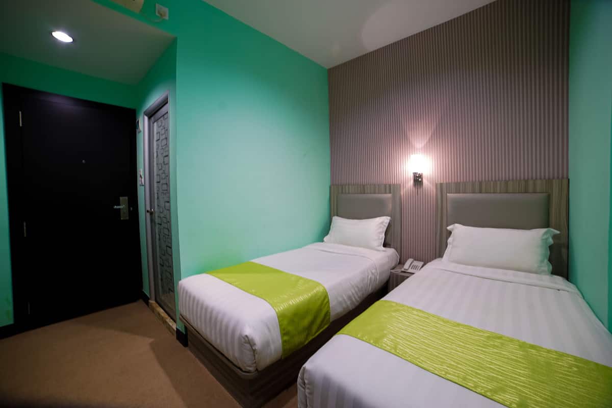 A hotel room with two beds, a door, and a nightstand with a phone.
