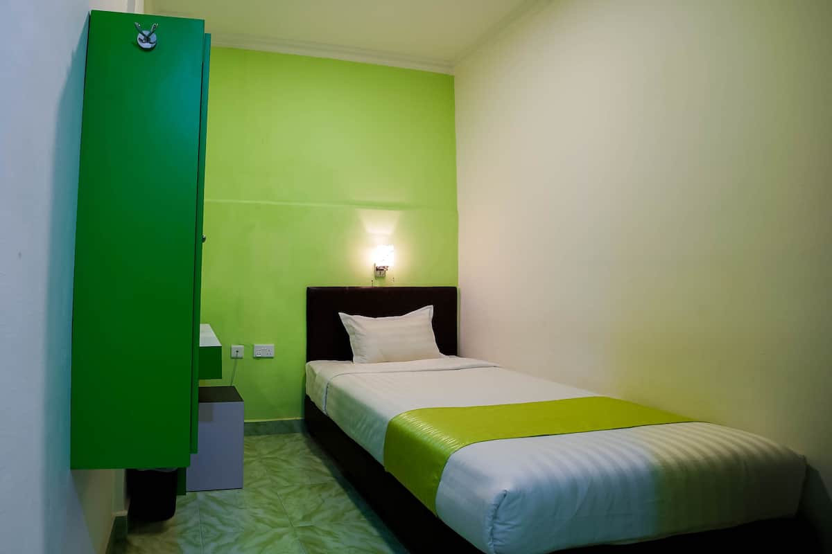 A single bed with a white and green bedspread, a black headboard, and a nightstand with a lamp.
