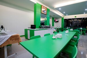 Un ristorante con tavoli e sedie verdi, un bancone con una macchina da caffè e un televisore fissato alla parete.
