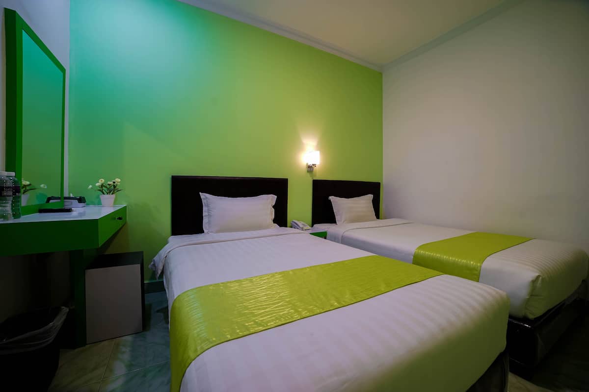 A hotel room with two beds, each with white bedding and green accents, a desk with a mirror, and a green wall.